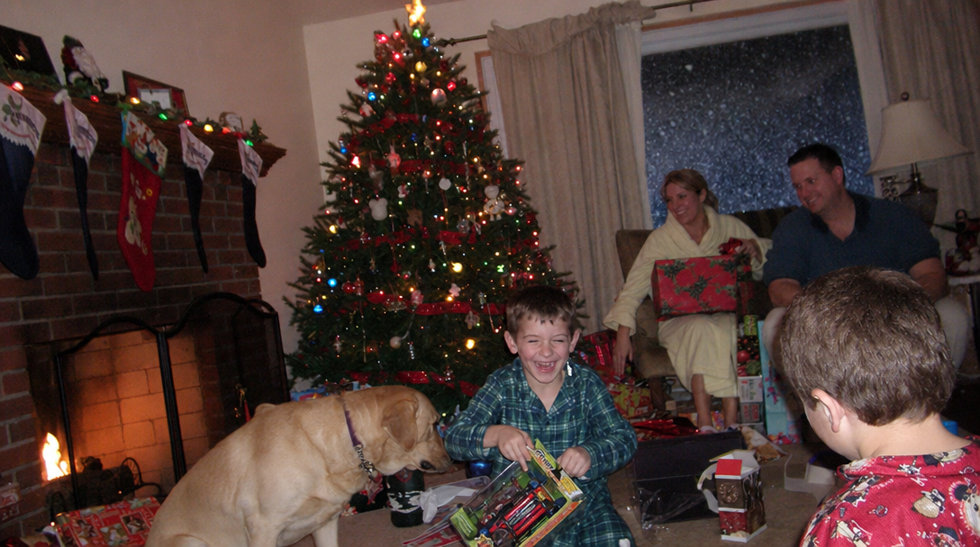 Mid-2000s family Christmas morning, kids tearing open presents under a heavily-decorated tree, golden lab puppy in the chaos, low-res digital camera flash photo, lived-in living room with stockings on the mantel.